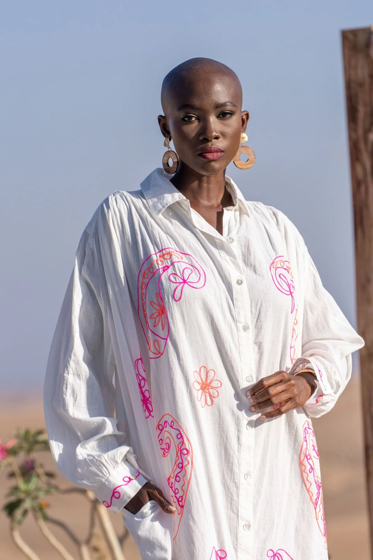 Woman wearing a white dress with pink patterns against a clear blue sky.