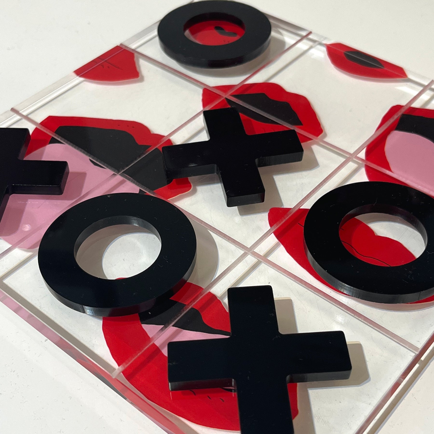 Tic-tac-toe game set with black and red pieces on a clear board.
