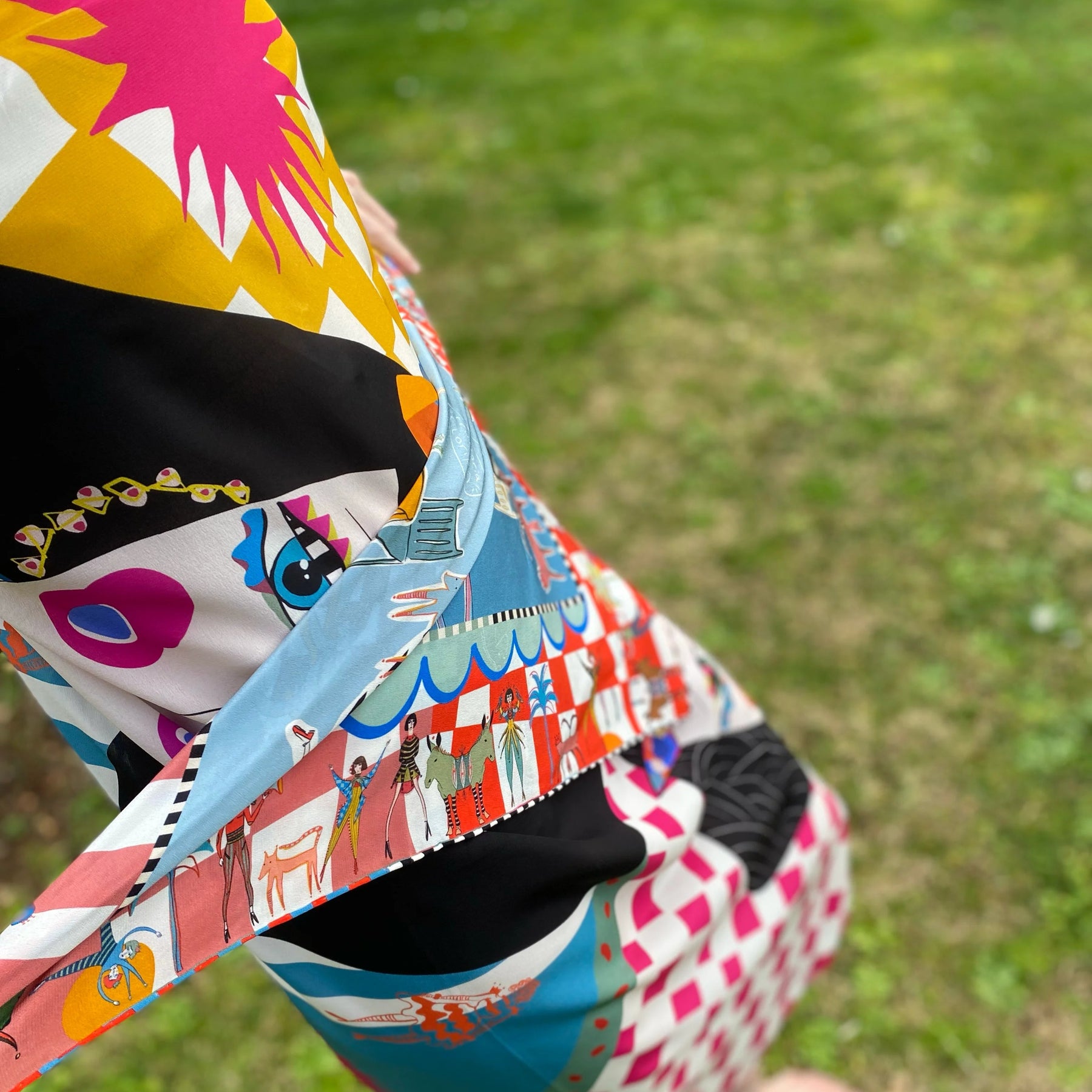 Person wearing a colorful outfit with a patterned headscarf on a grassy background