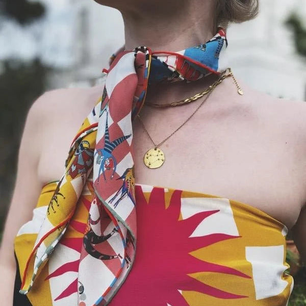 Person wearing a colorful scarf and top with a blurred outdoor background