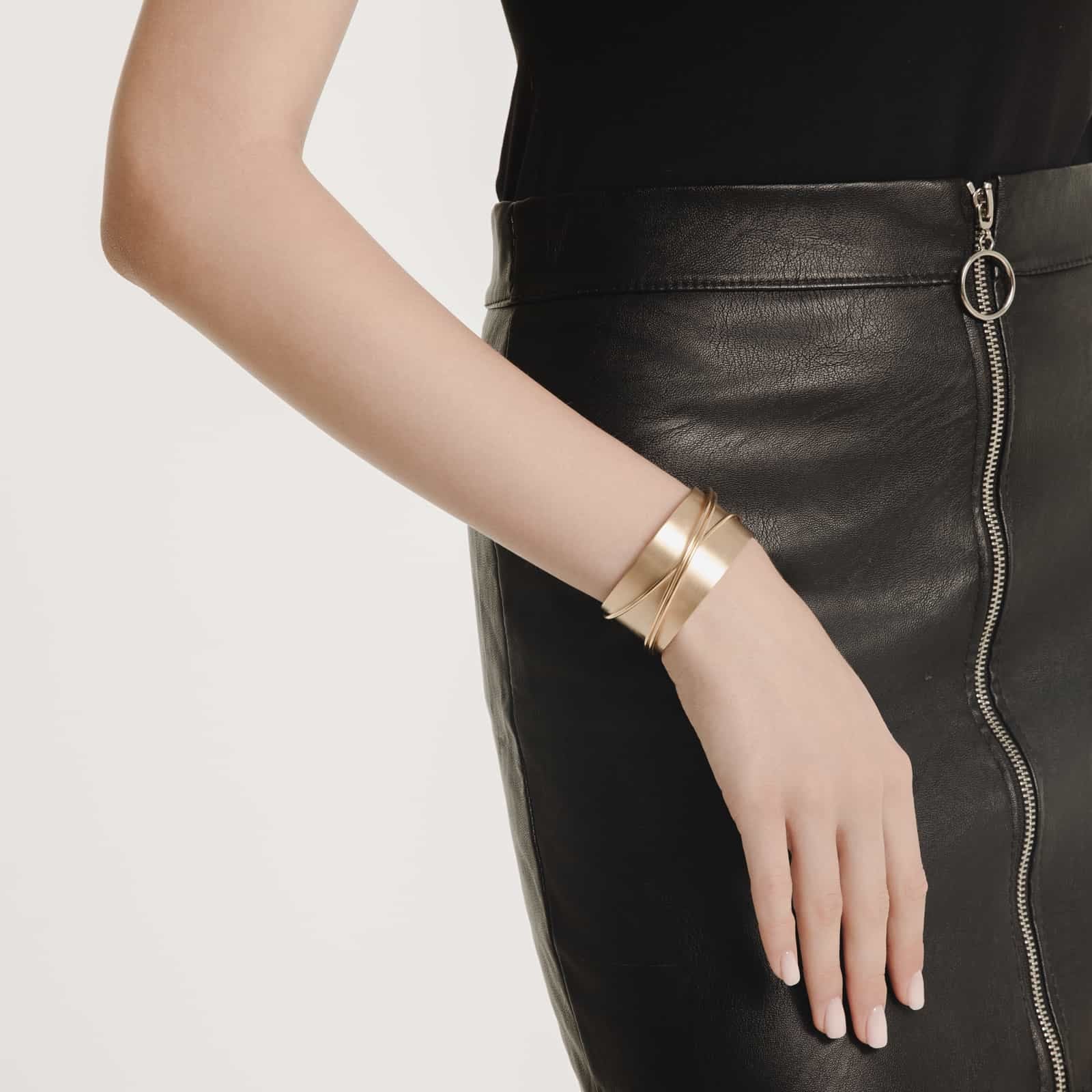 Person wearing a gold bracelet on a black leather skirt with a white background