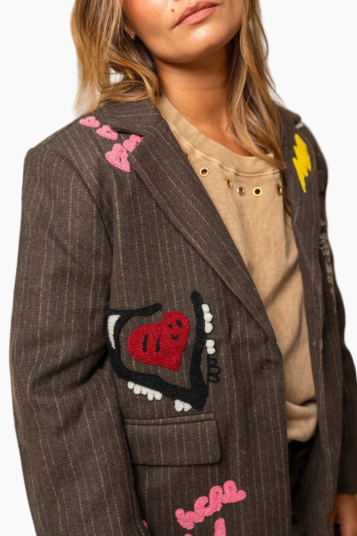 Person wearing a brown pinstripe blazer with colorful patches
