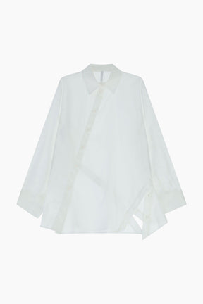  loose-fit shirt features an asymmetric back design highlighted by a distinctive diagonal button closure. A classic collar and long sleeves with cuffs frame a contemporary silhouette.