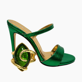 A single metallic green high-heeled sandal with an ankle strap and a decorative sculptural heel featuring a large green gemstone and gold chain detailing, shown on a plain white background.
