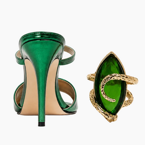 A pair of metallic emerald green high-heeled sandals shown from the back, alongside a matching green marquise-shaped ring with a gold snake-like band, on a clean white background.