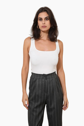 Woman wearing a white tank top and black pinstripe pants 