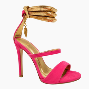 A single women's high-heeled sandal in bright pink suede with gold-tone metallic trim, a stacked ankle strap, and a dangling gold leaf charm, shown on a plain white background.