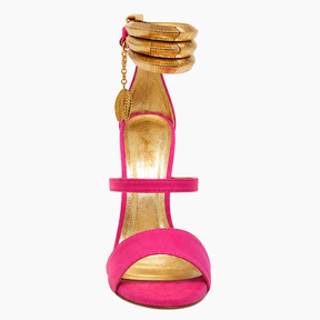 A single high-heeled sandal in bright pink suede with metallic gold accents, including a gold insole, gold platform toe, and a gold coiled ankle strap with a small gold leaf charm, shown against a plain white background.