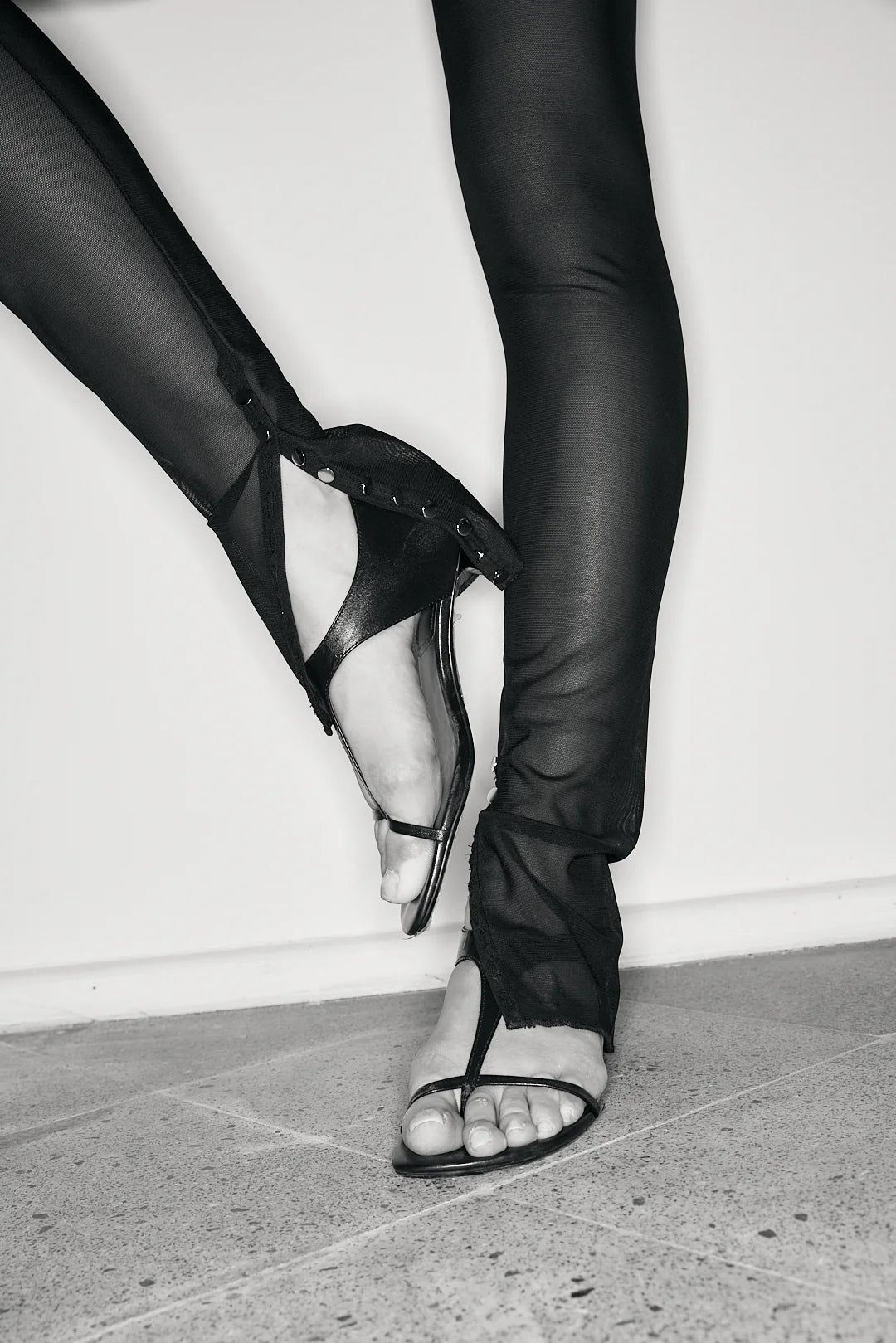 Person wearing black leather shoes and sheer black leggings