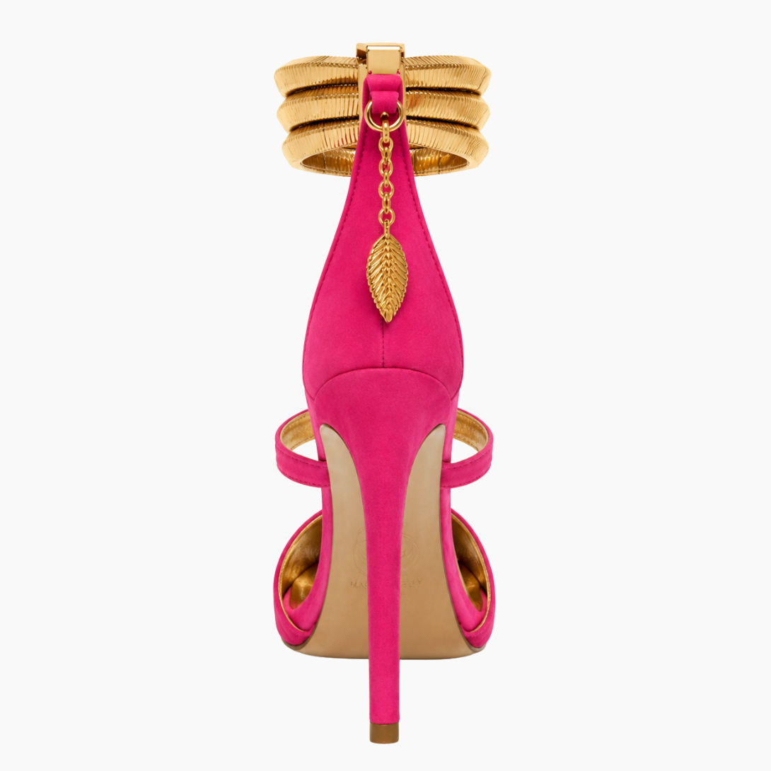 A single bright pink suede high-heeled sandal with gold-tone hardware, featuring an ankle strap with stacked gold bands, a hanging gold leaf charm, and a stiletto heel on a white background.