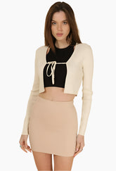 Woman wearing a black crop top, beige cardigan, and skirt 