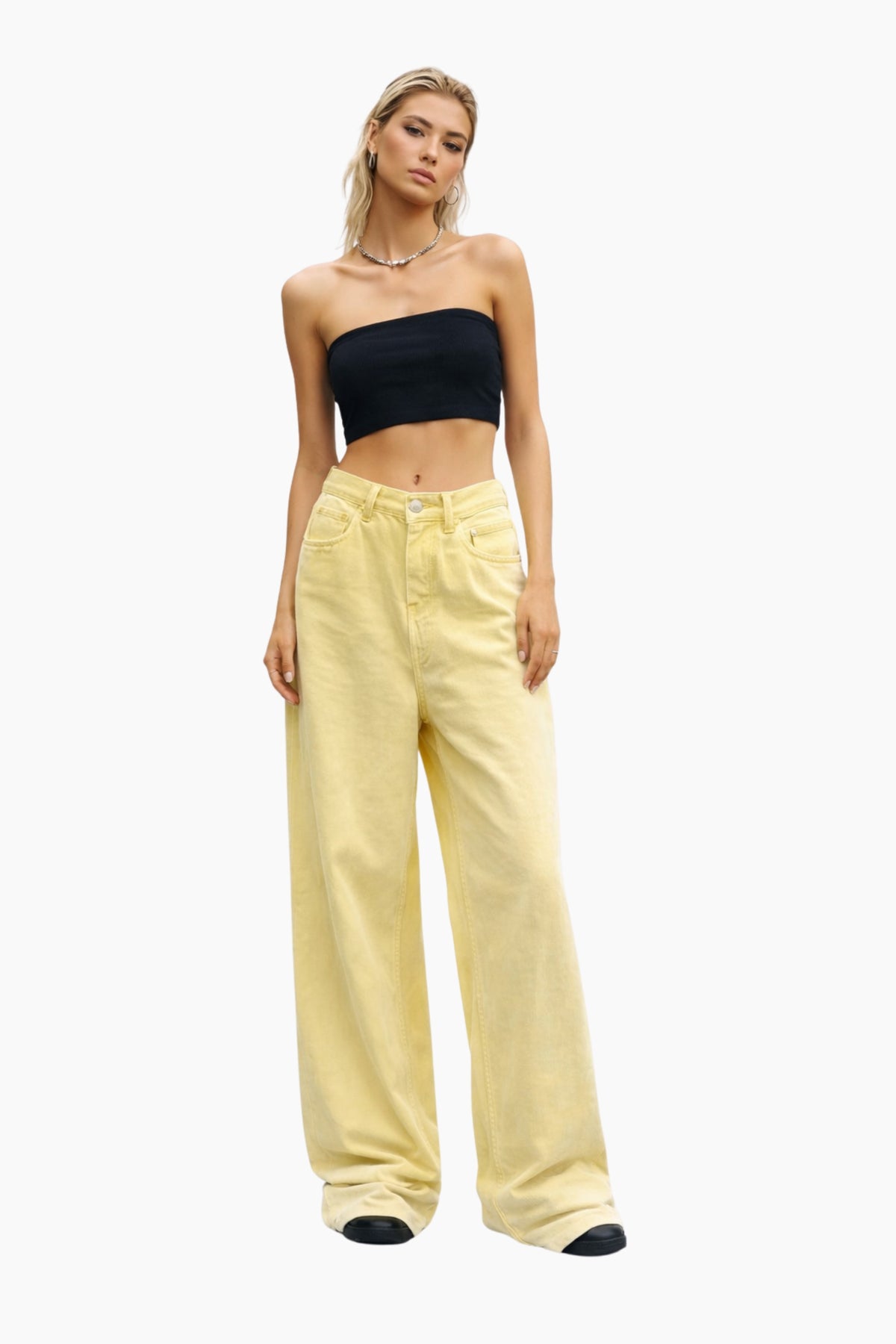 Woman wearing a black strapless top and yellow pants on a white background