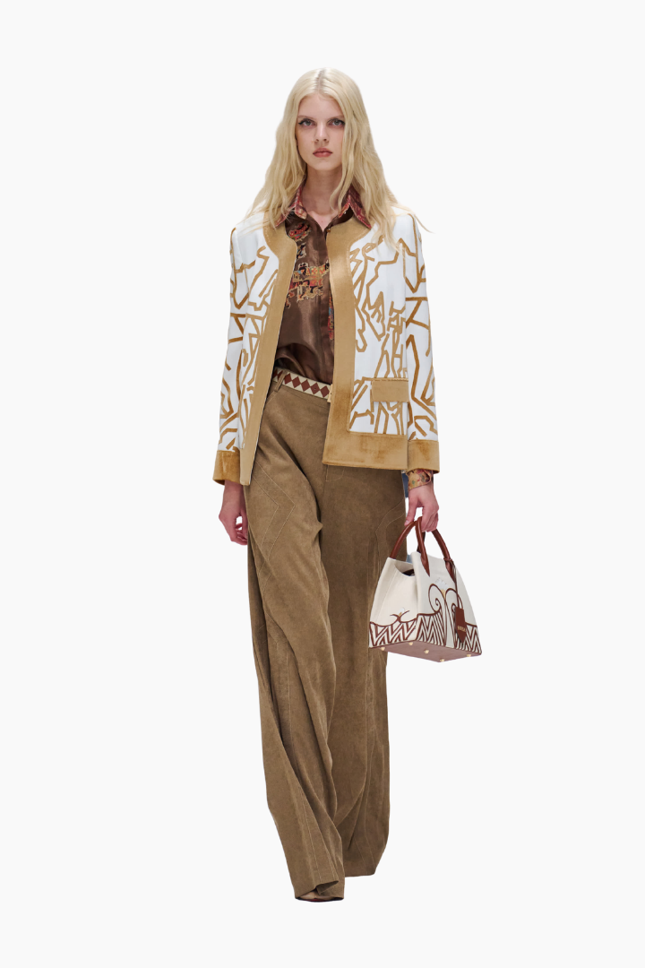 Woman wearing a vintage outfit with a jacket and pants, holding a matching handbag on a white background.