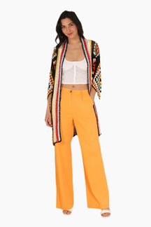 Woman wearing a colorful cardigan, white top, and yellow pants 