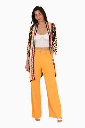 Woman wearing a colorful cardigan, white top, and yellow pants 