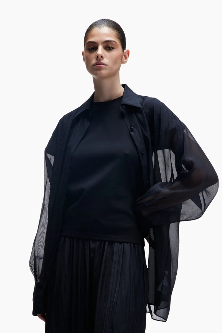 Woman wearing a black outfit with sheer sleeves on a white background