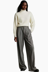 Person wearing a white turtleneck sweater and gray pants