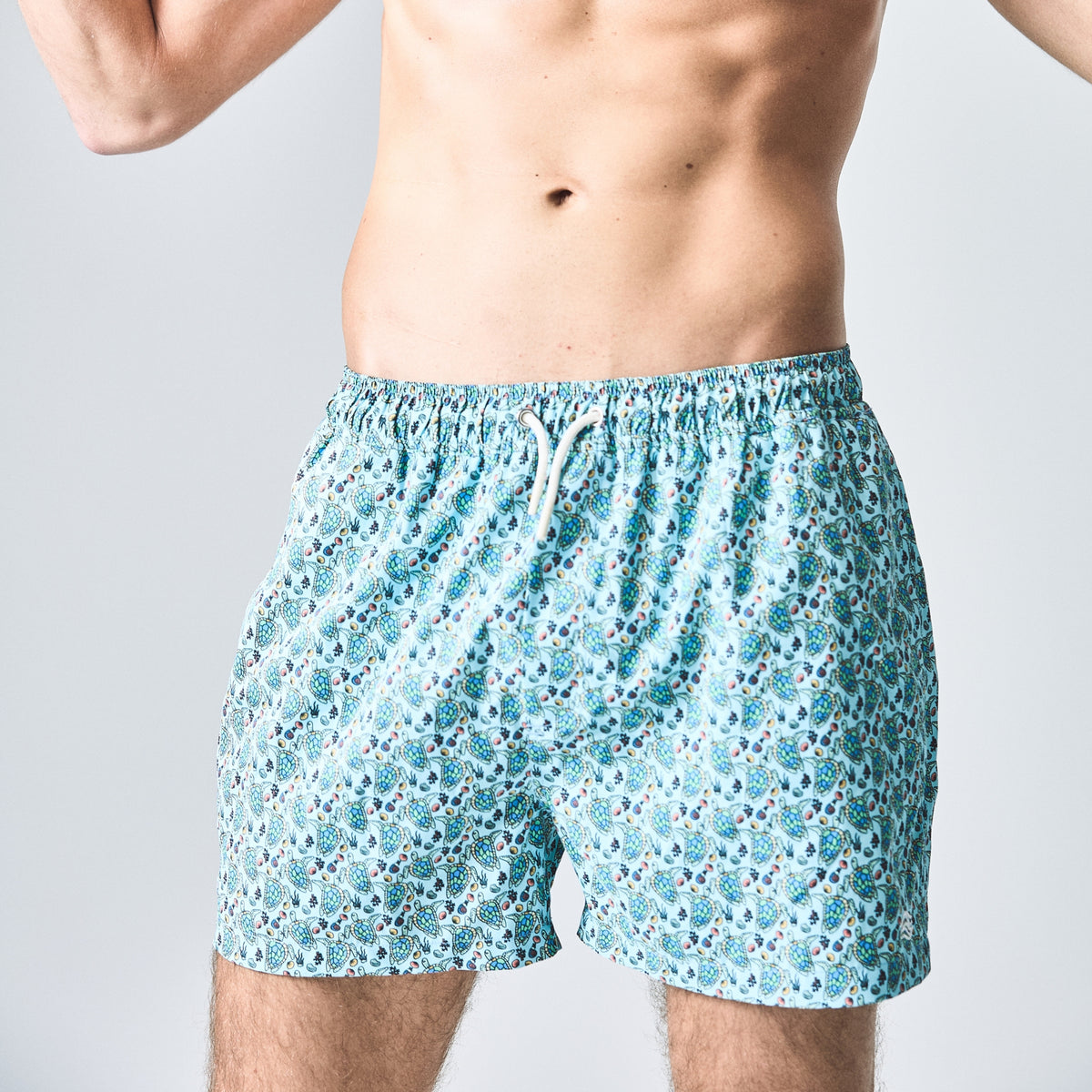 Teal floral-patterned swim shorts worn by a person on a light gray background