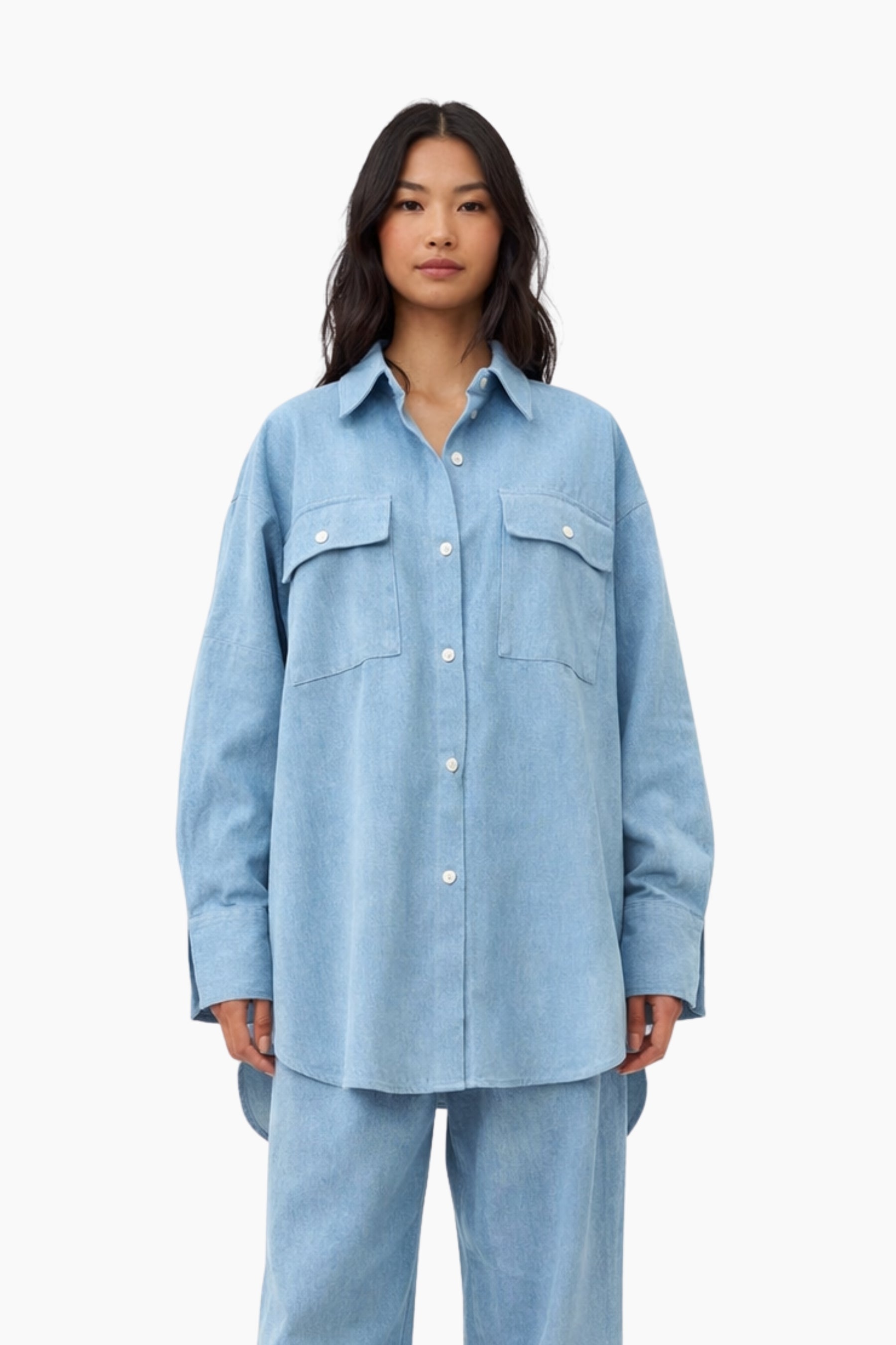 Woman wearing a light blue denim shirt and pants on a white background