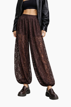 Person wearing brown lace pants with a black top and leather jacket on a white background