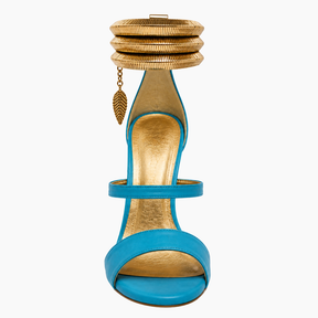 A single high-heeled sandal with a bright turquoise blue leather upper and a metallic gold footbed, featuring a stacked gold anklet-style strap with a small leaf charm on a light gray background.