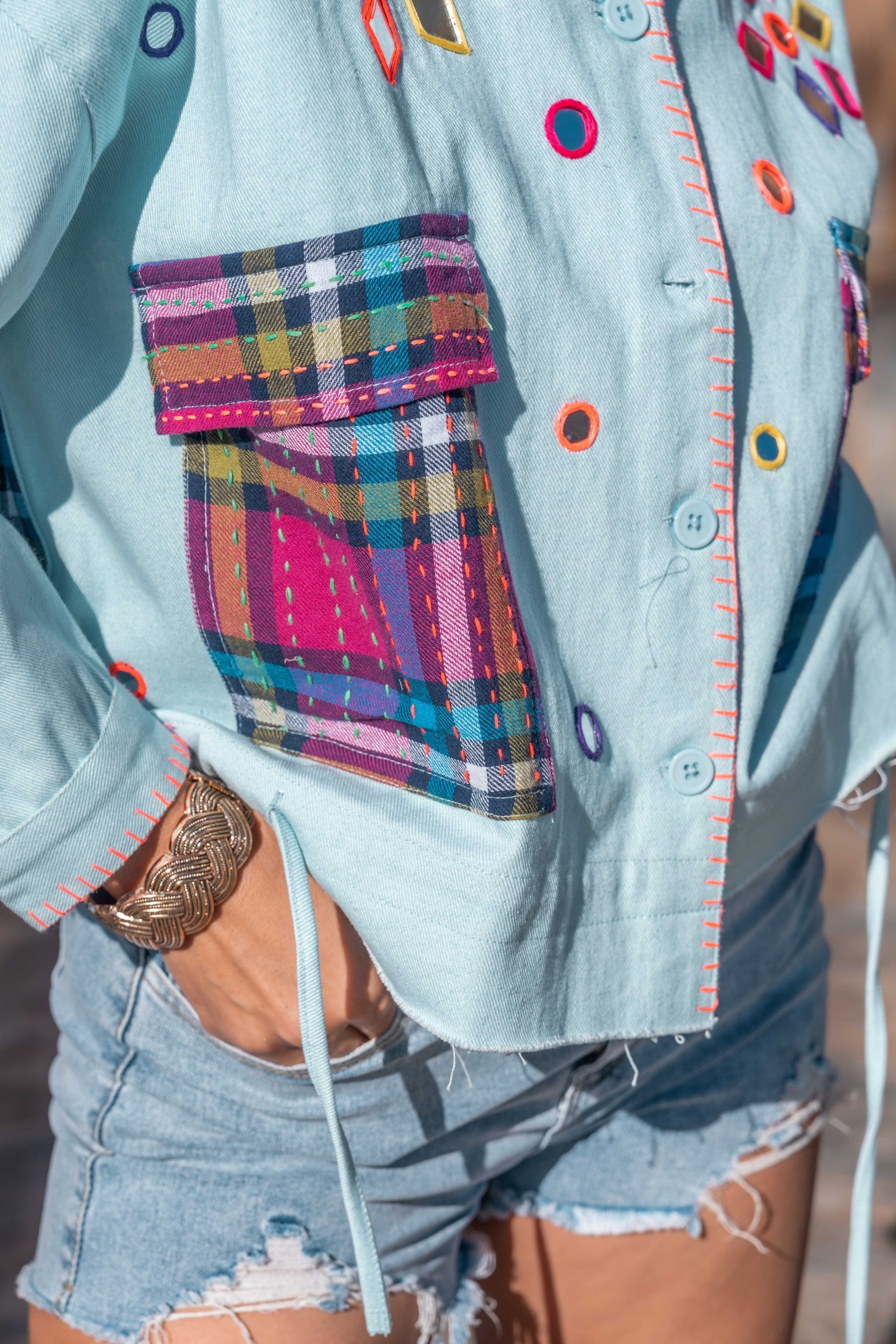 Light blue denim shirt with colorful buttons and plaid pocket, worn with denim shorts.