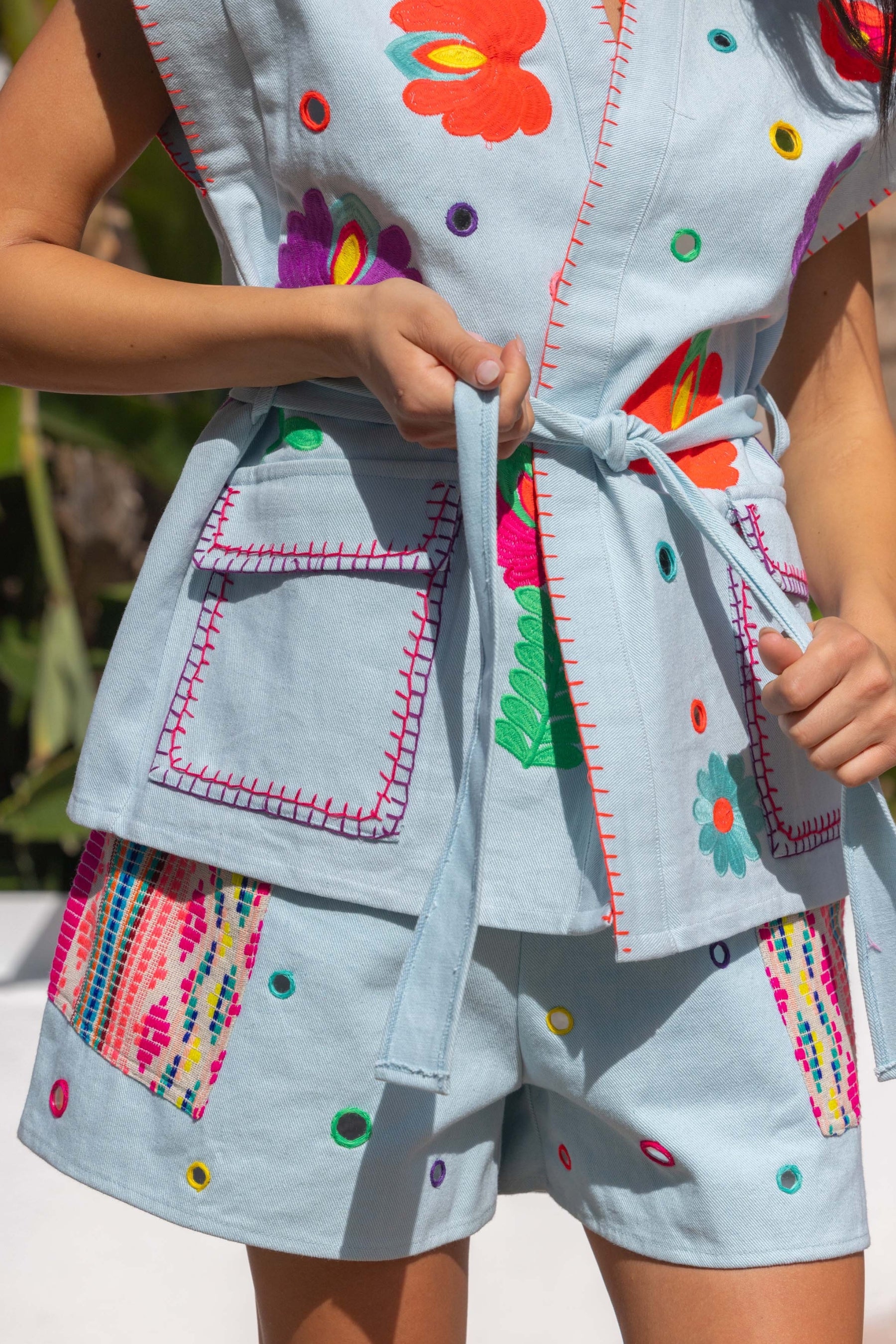 Children's outfit with colorful floral patterns and embroidery on a light blue background.
