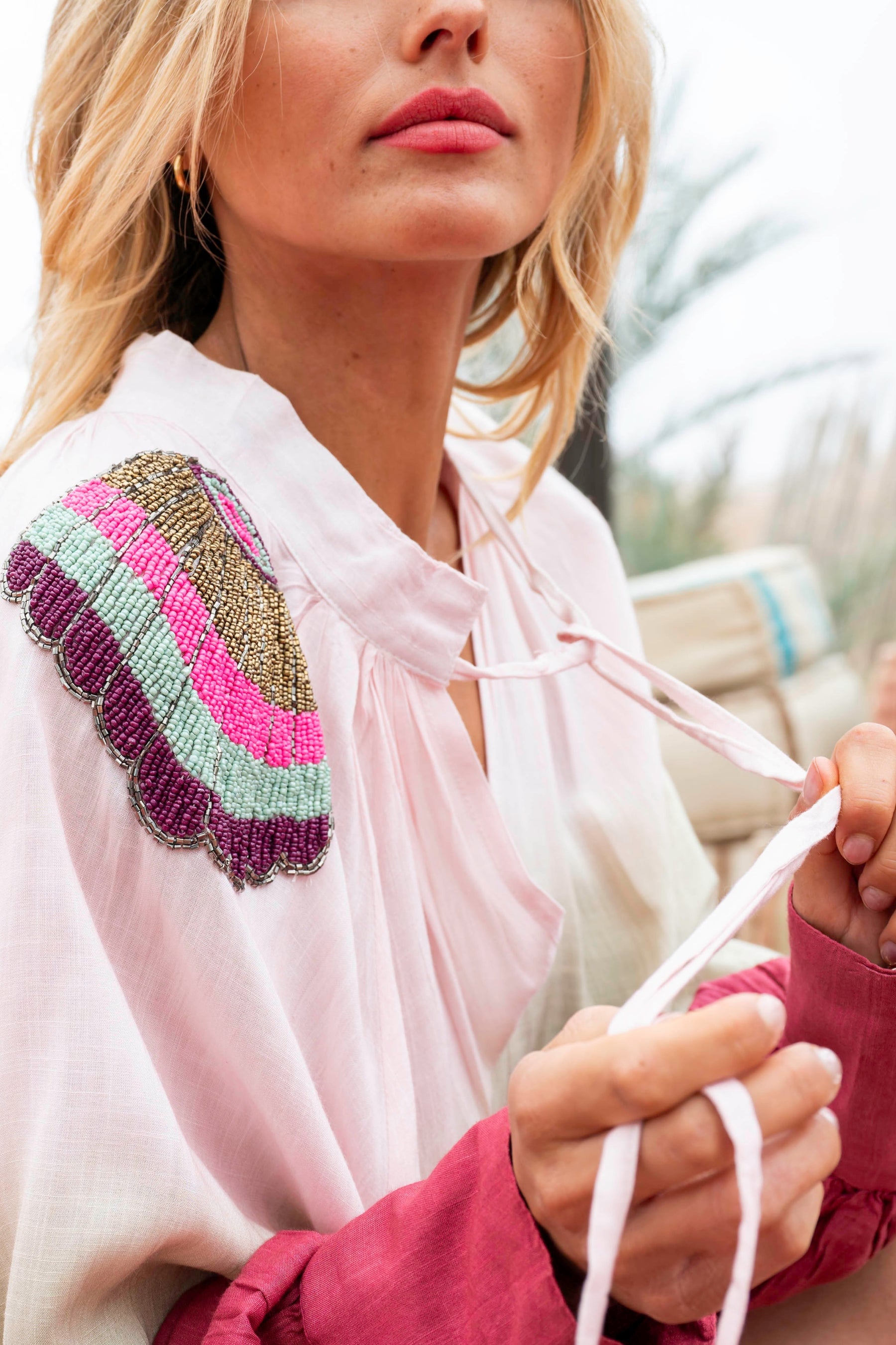 Woman wearing a pink blouse with a colorful embroidered sleeve, holding white strings.