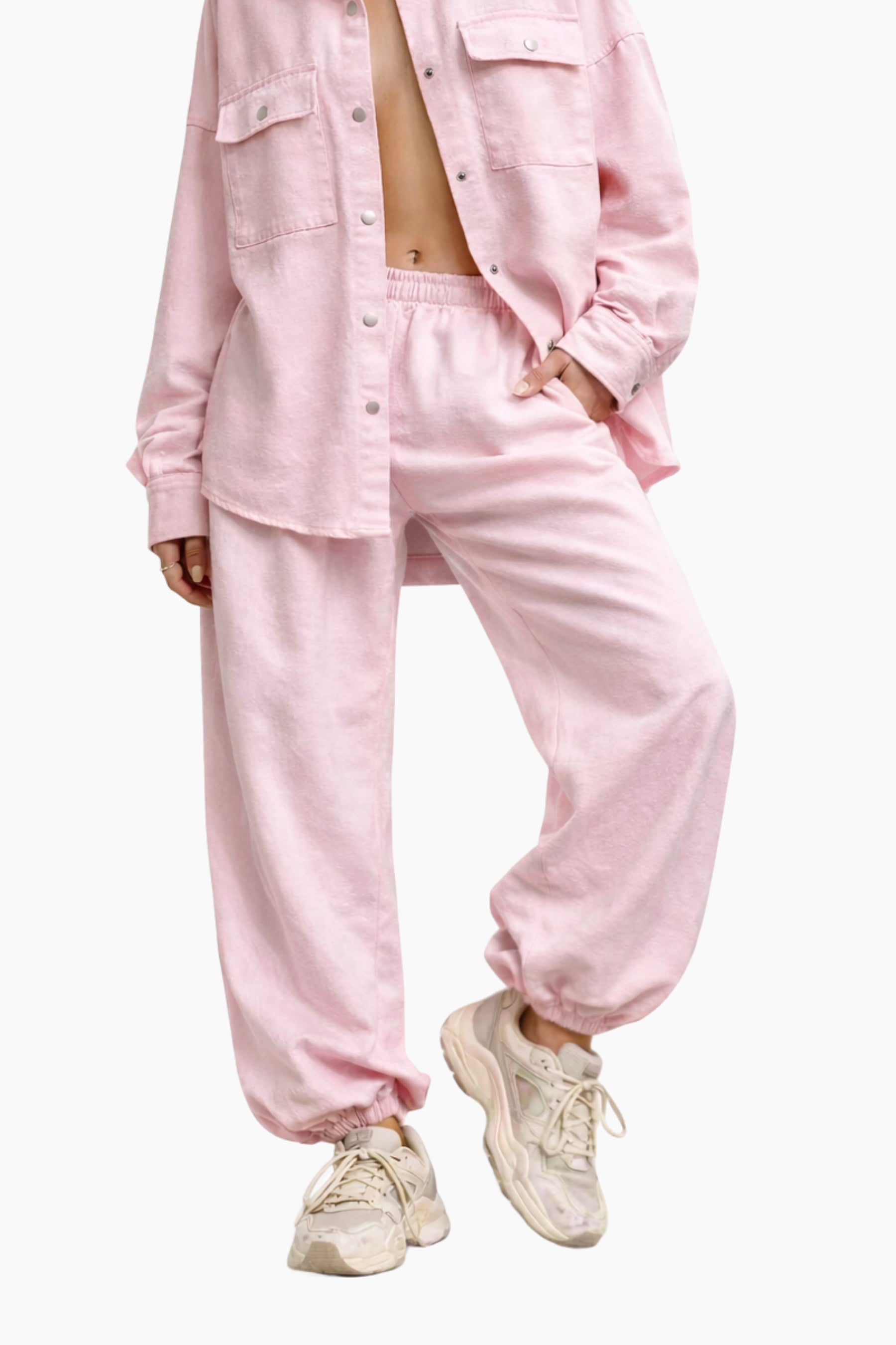 Person wearing a pink button-up shirt and pants with beige sneakers on a white background