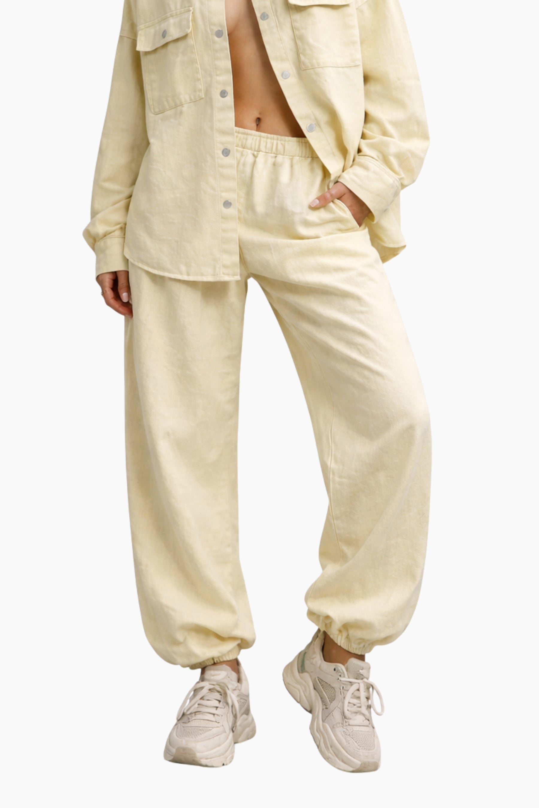 Person wearing a beige button-up shirt and pants with white sneakers on a white background