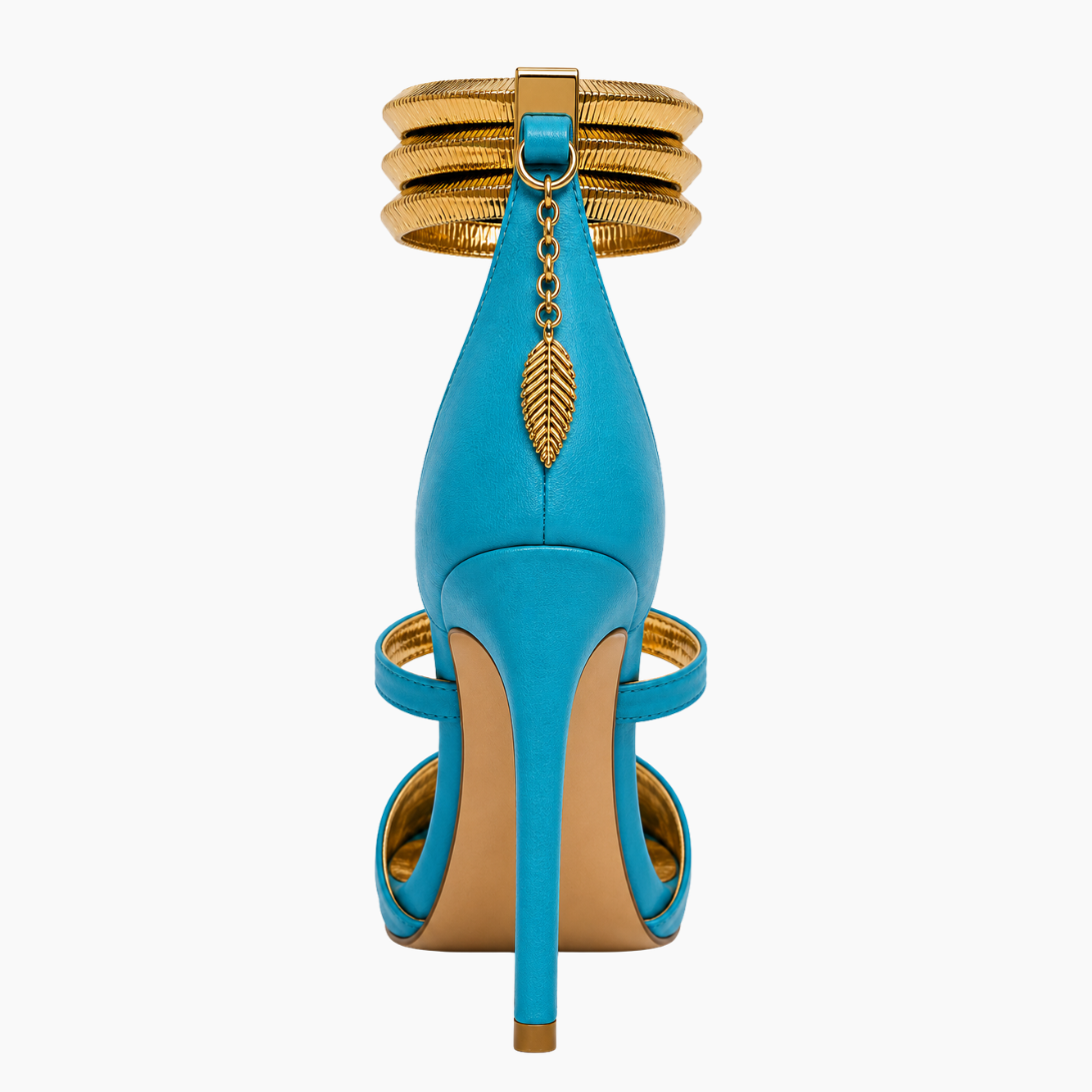 A single high-heeled sandal shown from the back on a light gray background. The shoe features a bright turquoise blue leather body with gold-tone metal accents, including stacked rings on the ankle strap, a hanging leaf charm, and a tan/beige insole.