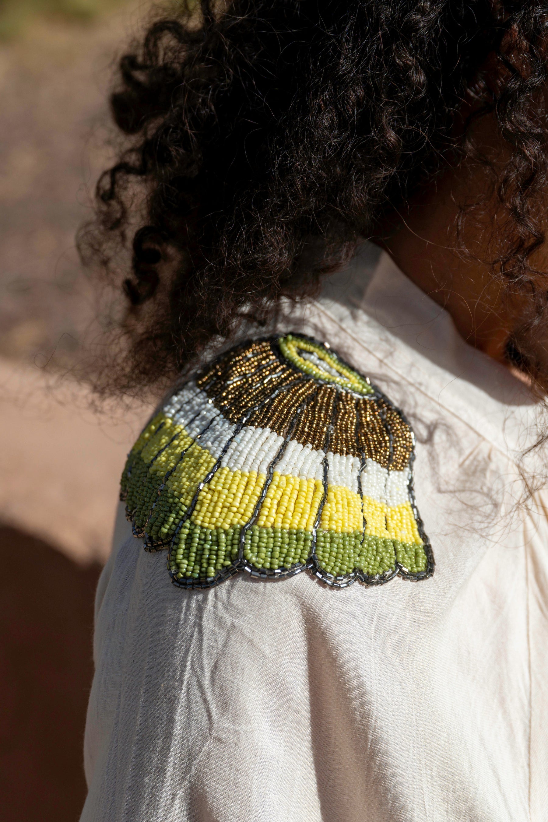 Close-up of a person wearing a white garment with a green and yellow beaded butterfly design on the shoulder.