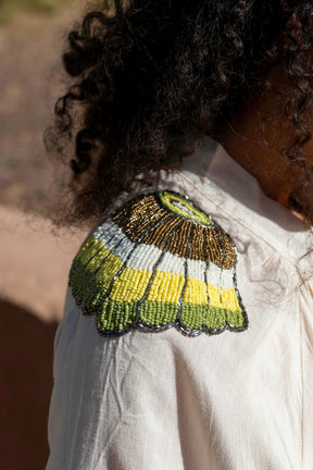 Close-up of a person wearing a white garment with a green and yellow beaded butterfly design on the shoulder.