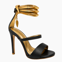 A black leather high-heeled sandal with a gold metallic textured ankle strap, gold interior lining, and a gold leaf charm, shown against a plain white background.