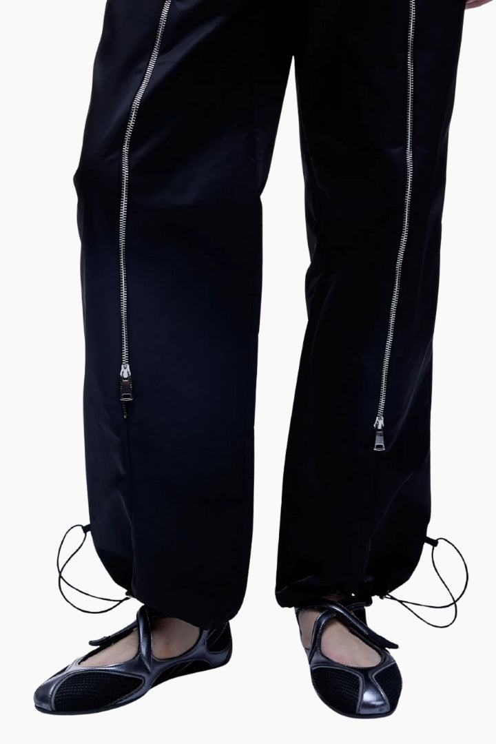Black pants with silver zippers worn by a person on a white background