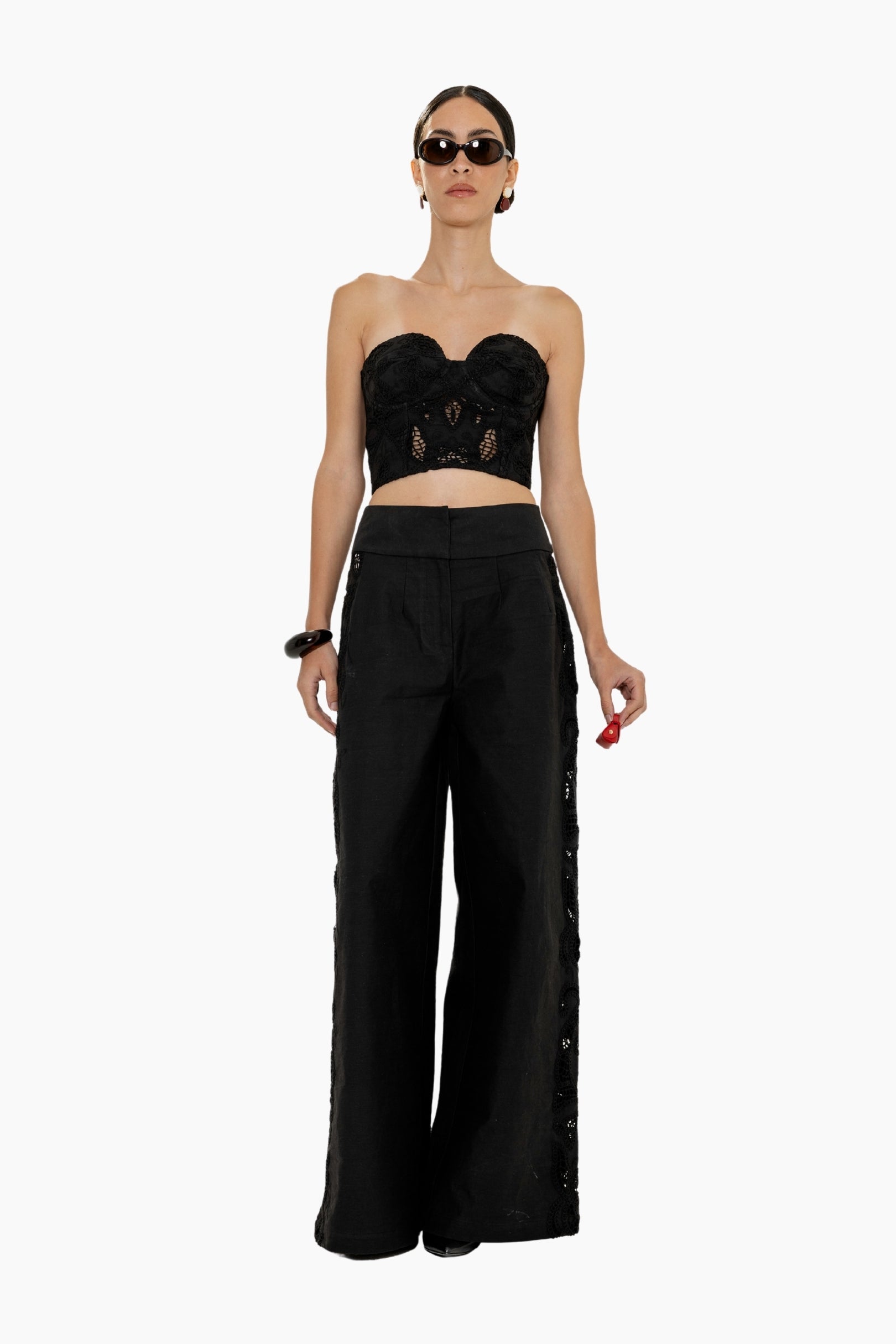 Woman wearing a black strapless top and a High-waisted black trousers featuring bold floral cutwork panels along the sides.