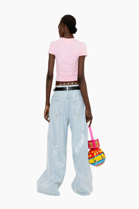 Person wearing a pink top and light blue jeans, holding a colorful bag 