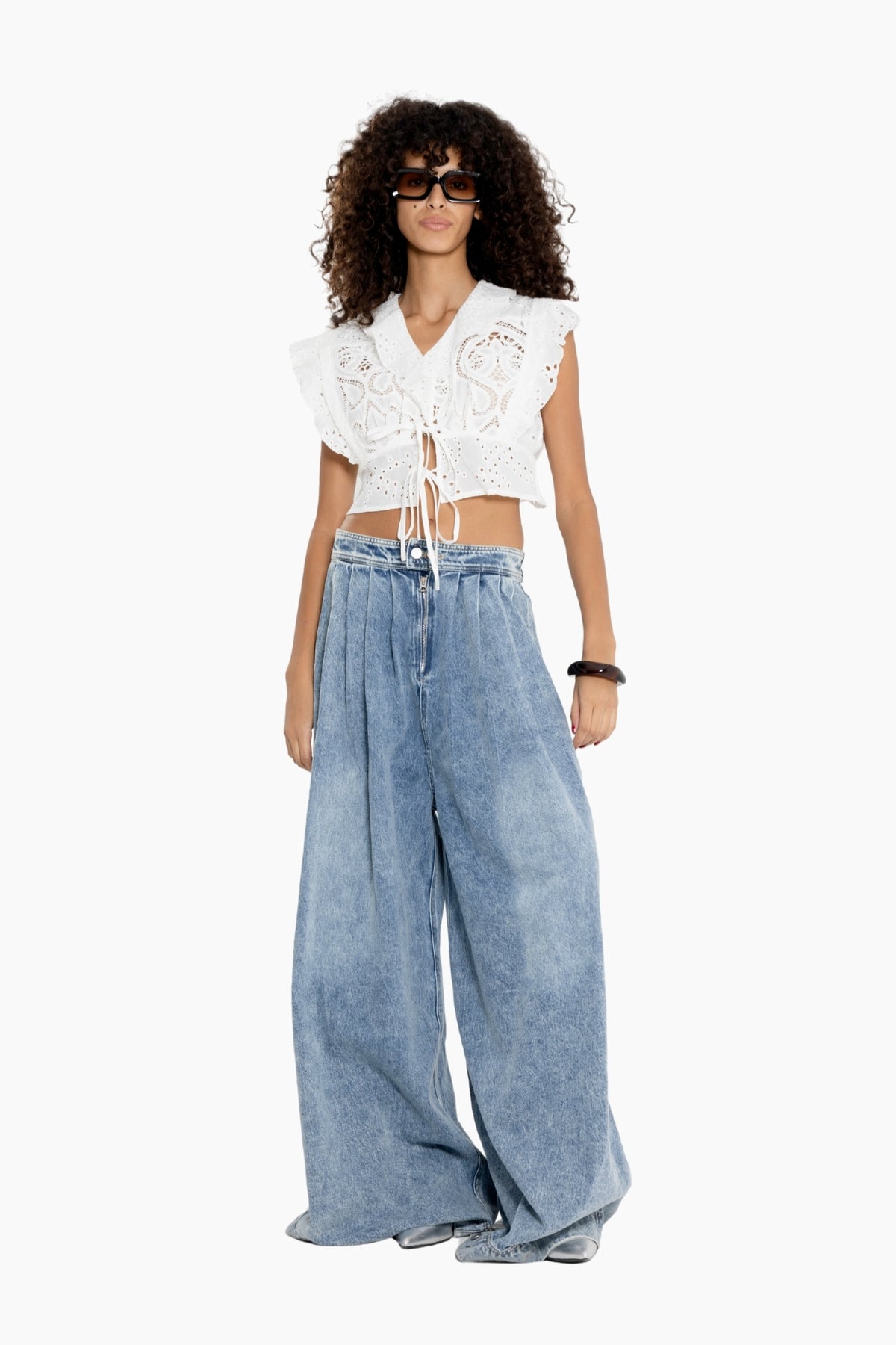 Woman wearing a white lace top and wide-leg blue jeans on a white background