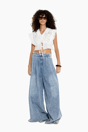 Woman wearing a white lace top and wide-leg blue jeans on a white background