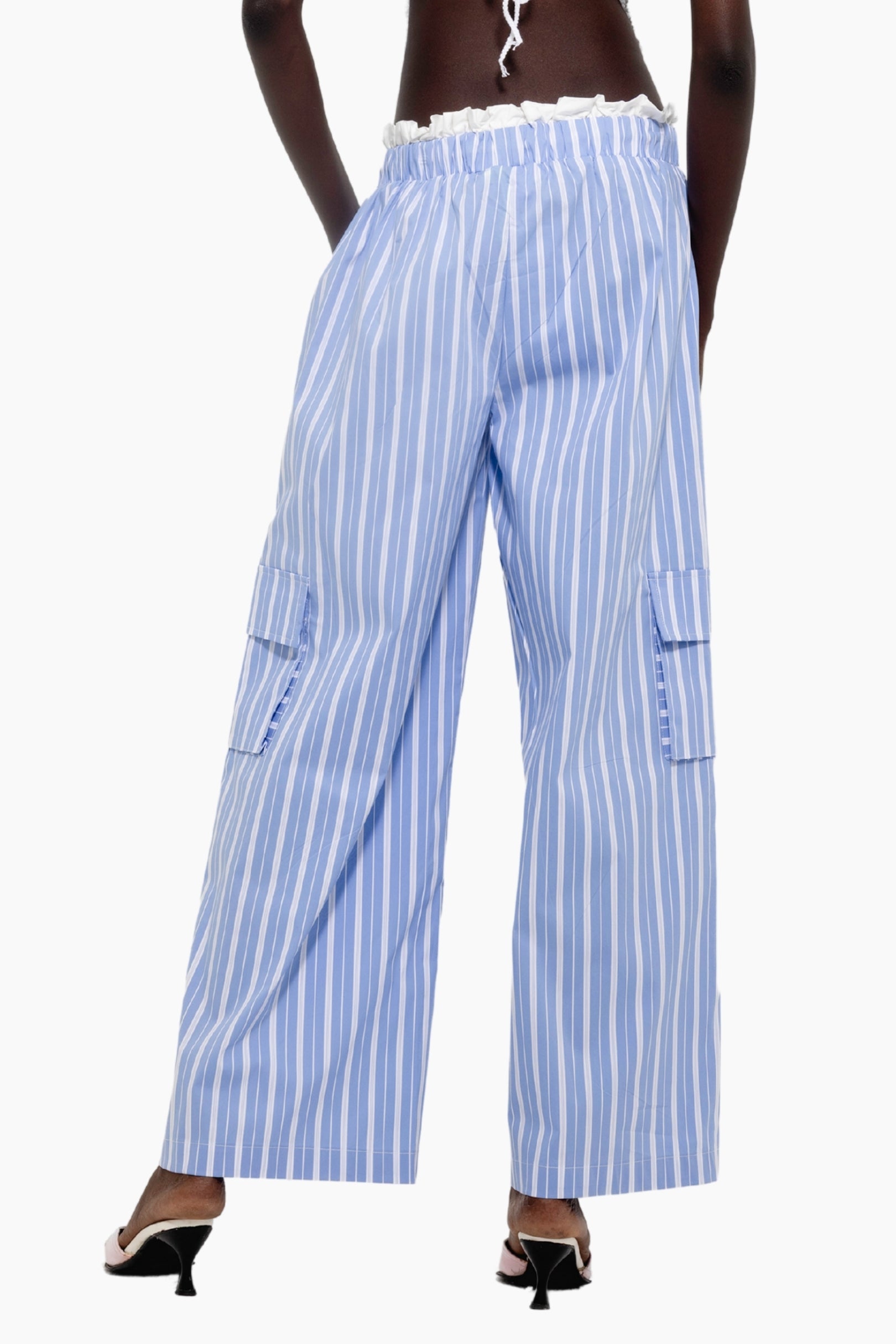Woman wearing a white top and Light blue and white cargo-style trousers with vertical stripes and side flap pockets.