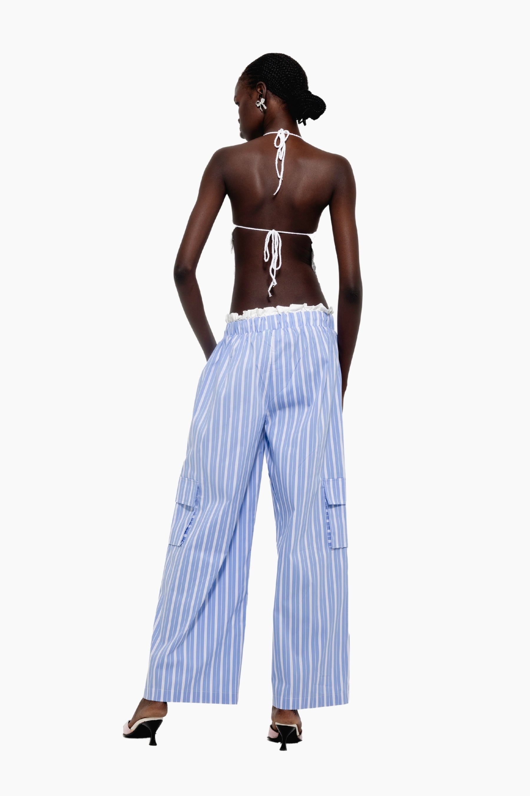 Woman wearing a white top and Light blue and white cargo-style trousers with vertical stripes and side flap pockets.