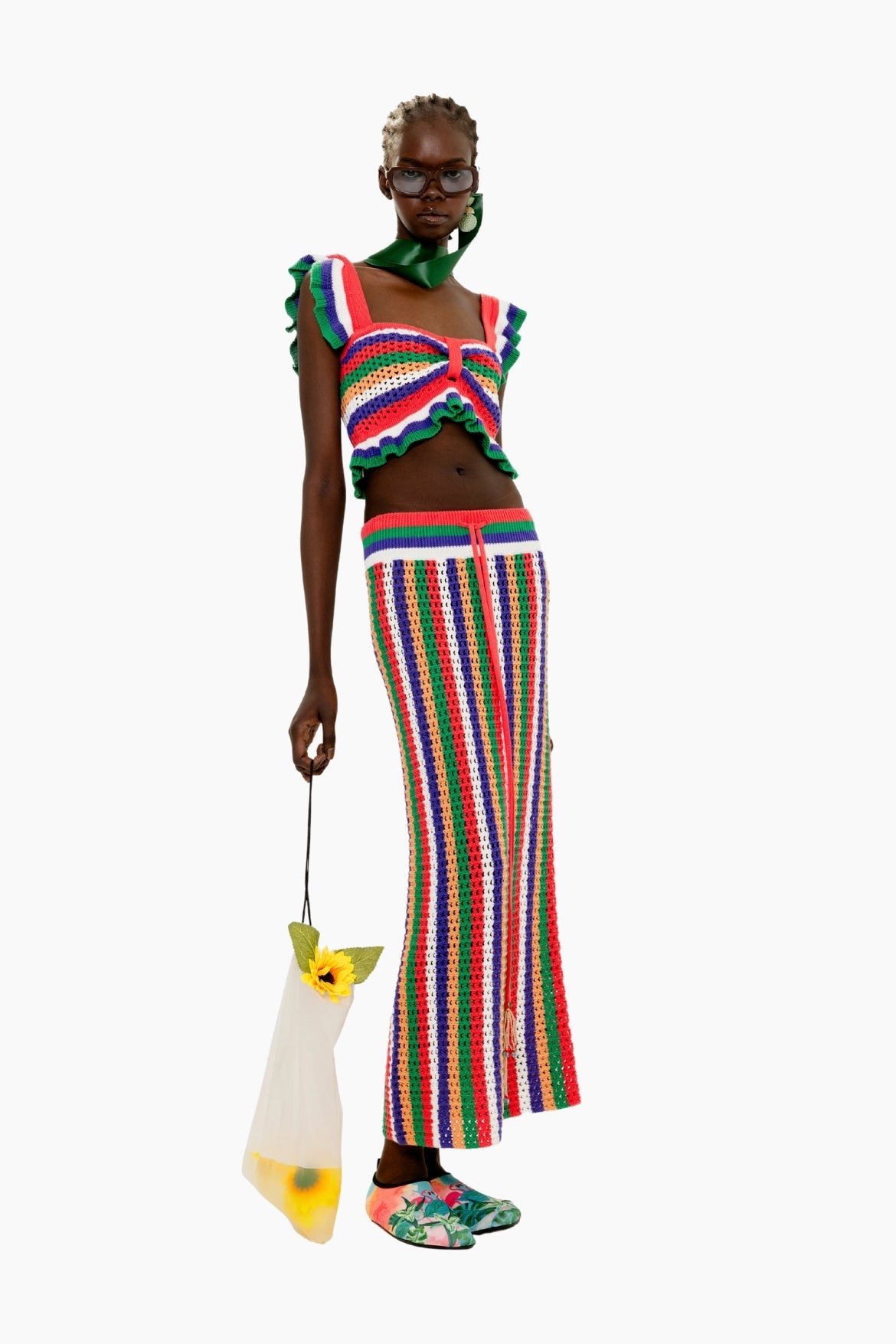 Model wearing a colorful outfit with a striped skirt and top, holding a yellow bag.