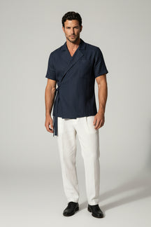 Man wearing a navy shirt and white pants against a gray background