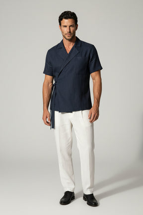 Man wearing a navy shirt and white pants against a gray background
