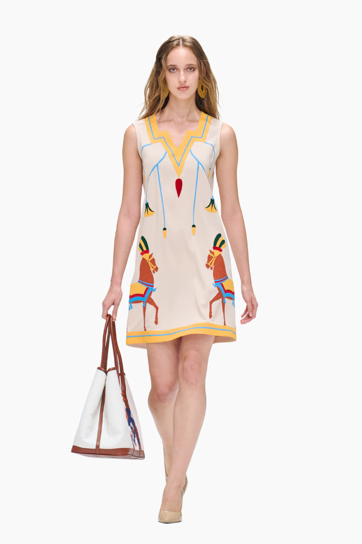 Woman wearing a colorful dress with horse designs, holding a white bag with brown handles.