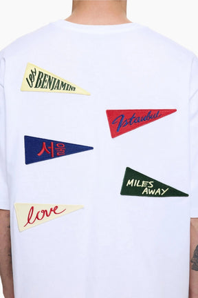 White t-shirt with colorful pennant flags and text on a person wearing it.