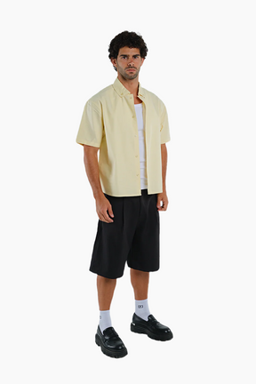 Man wearing a light yellow shirt, black shorts, and black shoes