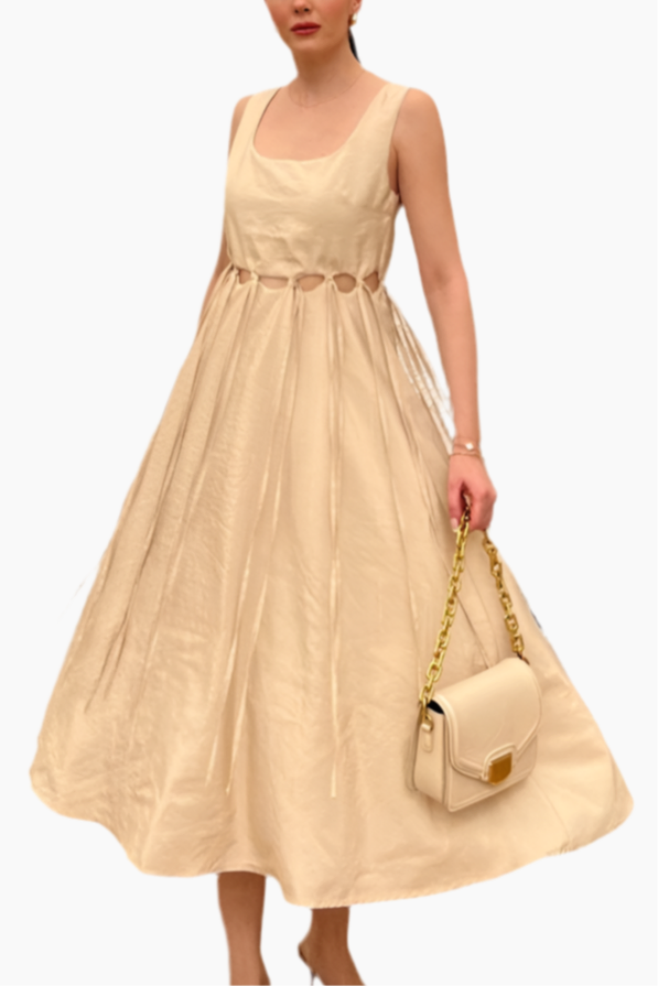 Woman wearing a beige dress holding a matching handbag on a white background