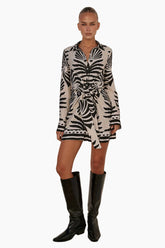 Model wearing a short dress with long sleeves featuring button closure with black knee-high boots 