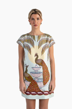 Woman wearing a dress with peacock and fountain design on a white background